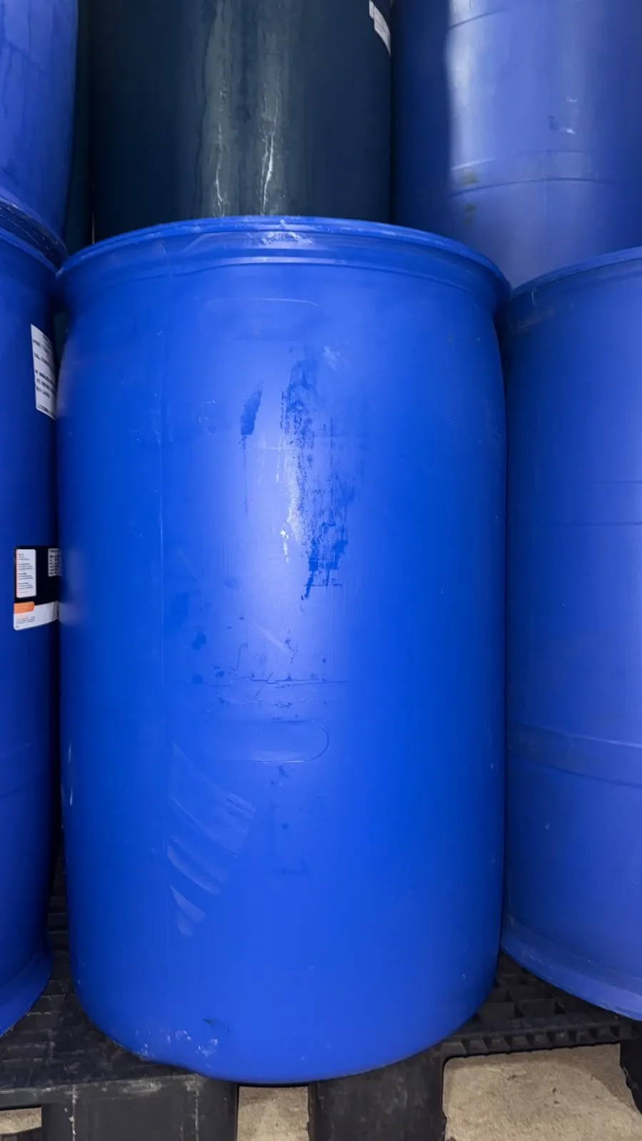 Bombona plástica azul de 200 litros reutilizada, sobre pallet no pátio