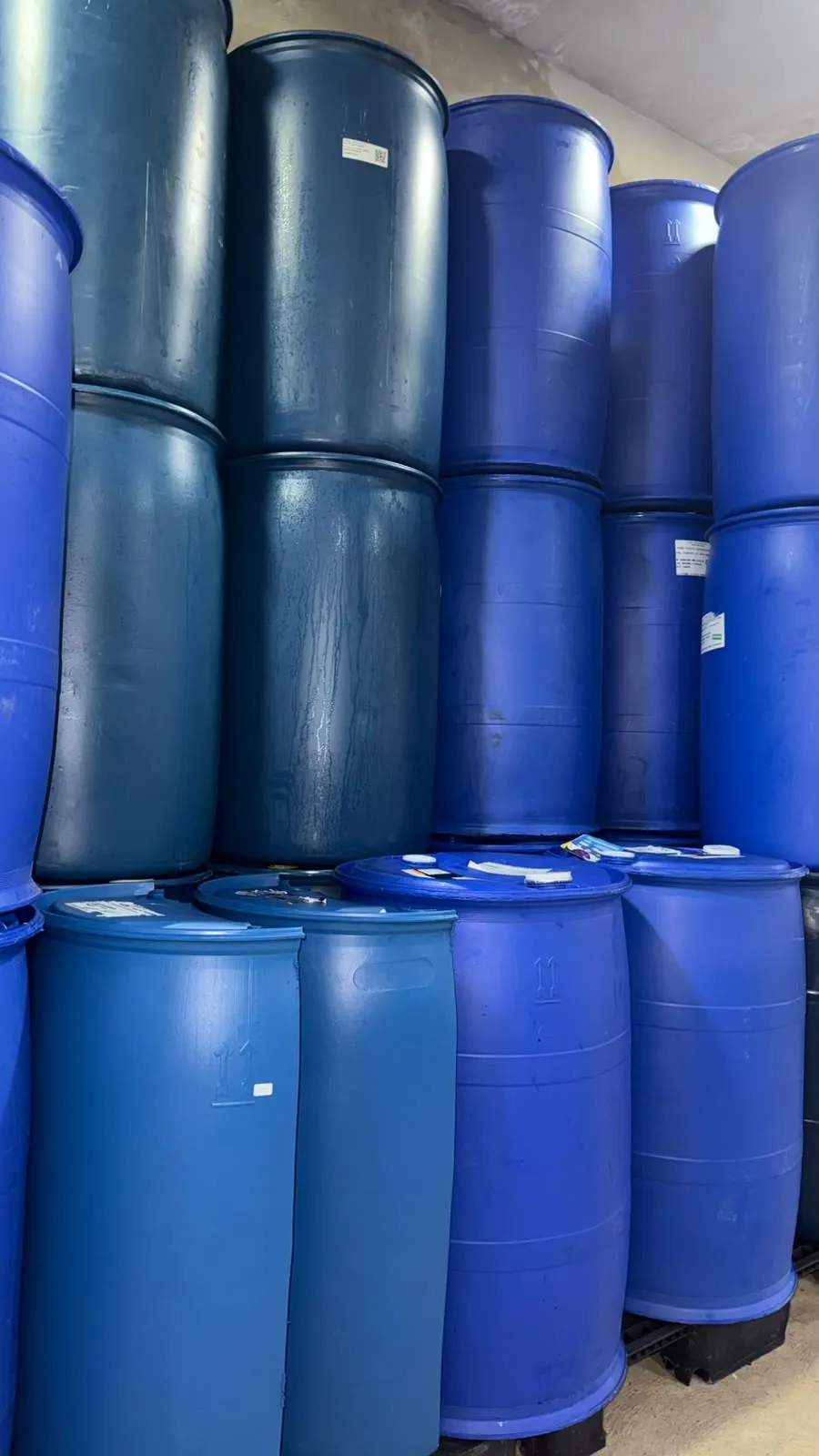 Tambores plásticos de 200 litros azuis usados, empilhados no estoque da Joel Tambores