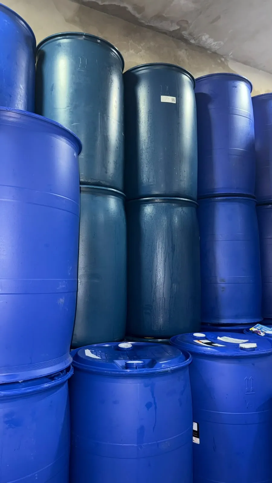 Bombonas plásticas azuis de 50 litros com alça e tampa, empilhadas no pátio